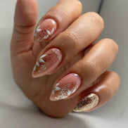Hand wearing peach almond press-on nails with white floral art and rose gold glitter tips